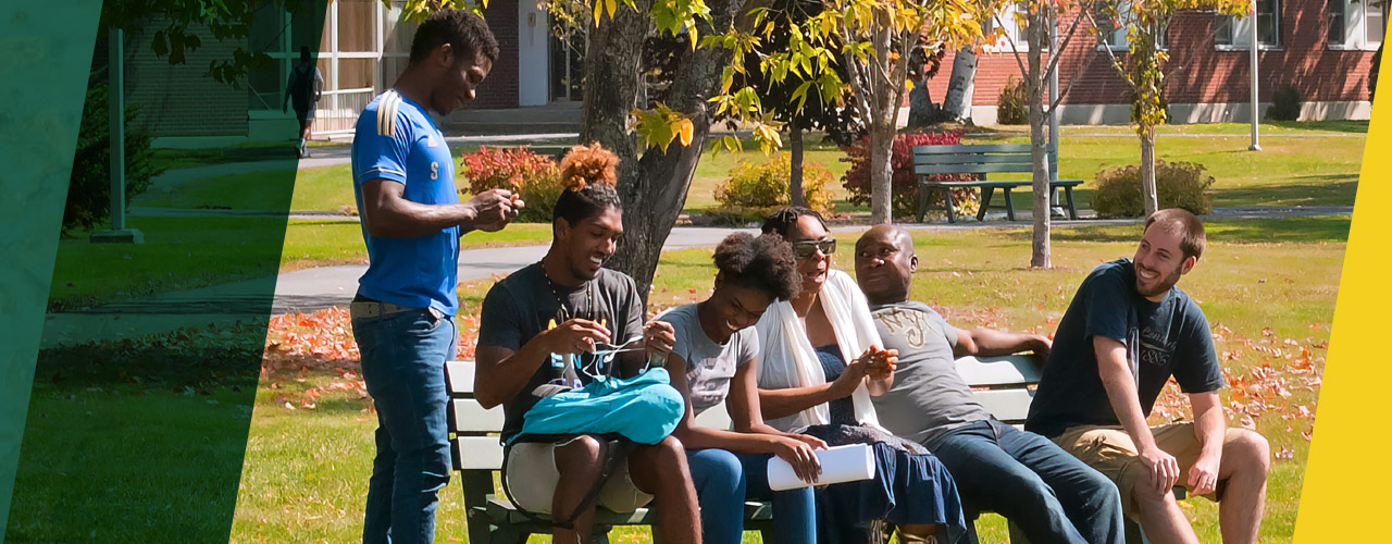 a diverse group of students gather and converse, sitting on a bench in the quad near Cyr Hall