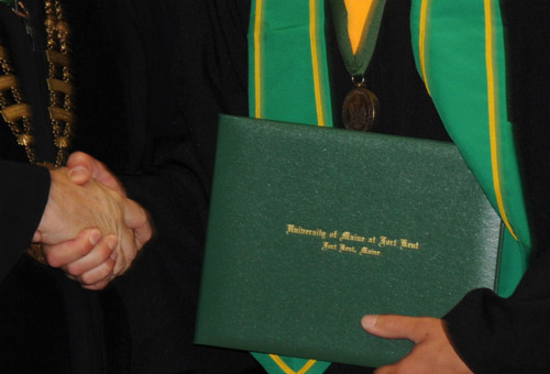 UMFK graduate holding his diploma and shaking the President's hand