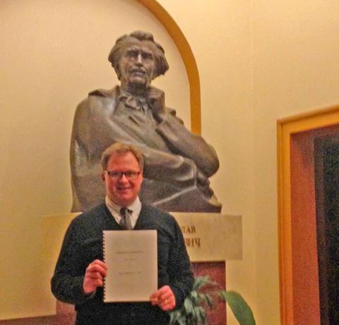 UMFK Professor Scott Brickman stands holding a copy of his composition 