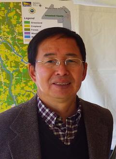 headshot of Dr. Chunzeng Wang, Ph.D., standing in front of a map of Aroostook county