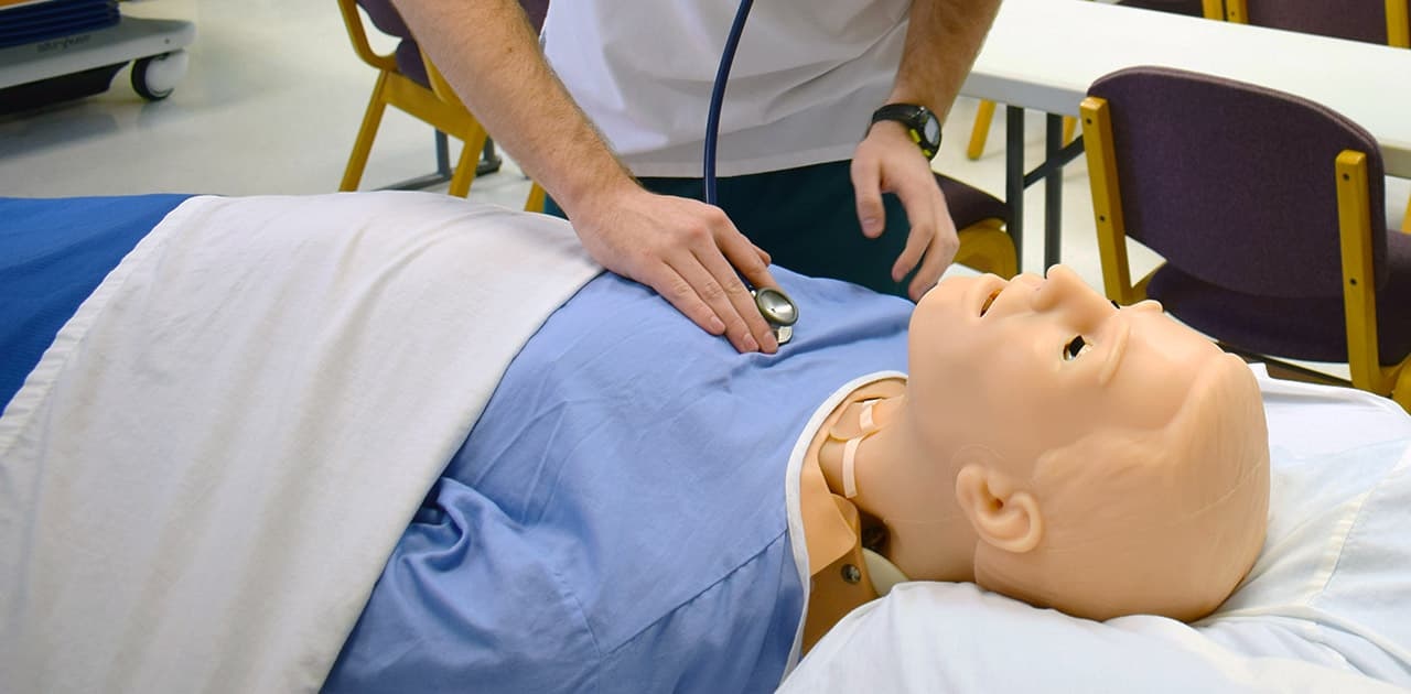 a student practices listening to a patient's lungs using a practice mannequin