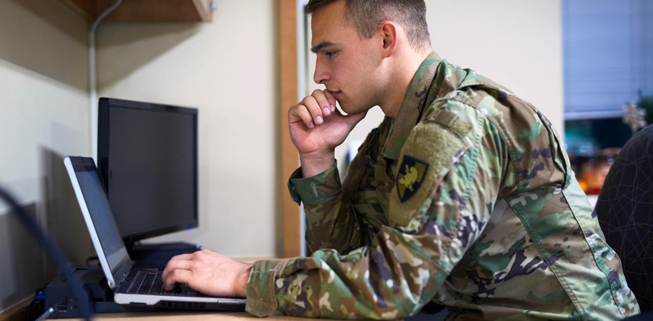 soldier in army fatigues sits at a computer reading something online