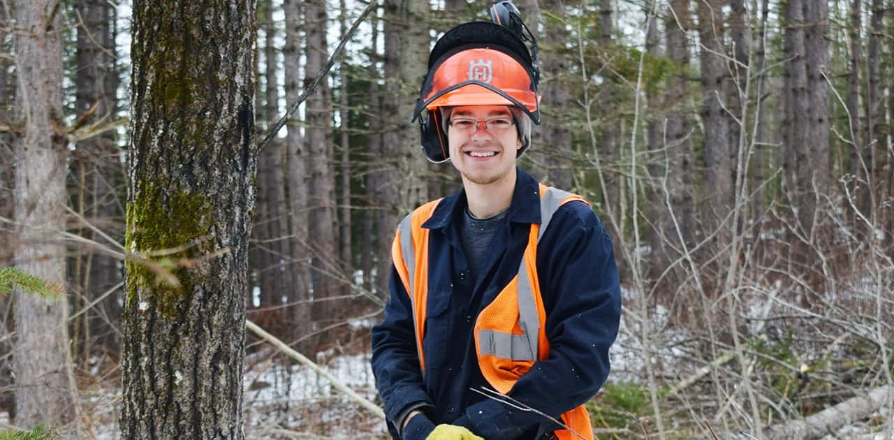 forestry student Alex Gillis stands in a forest wearing forestry safety gear