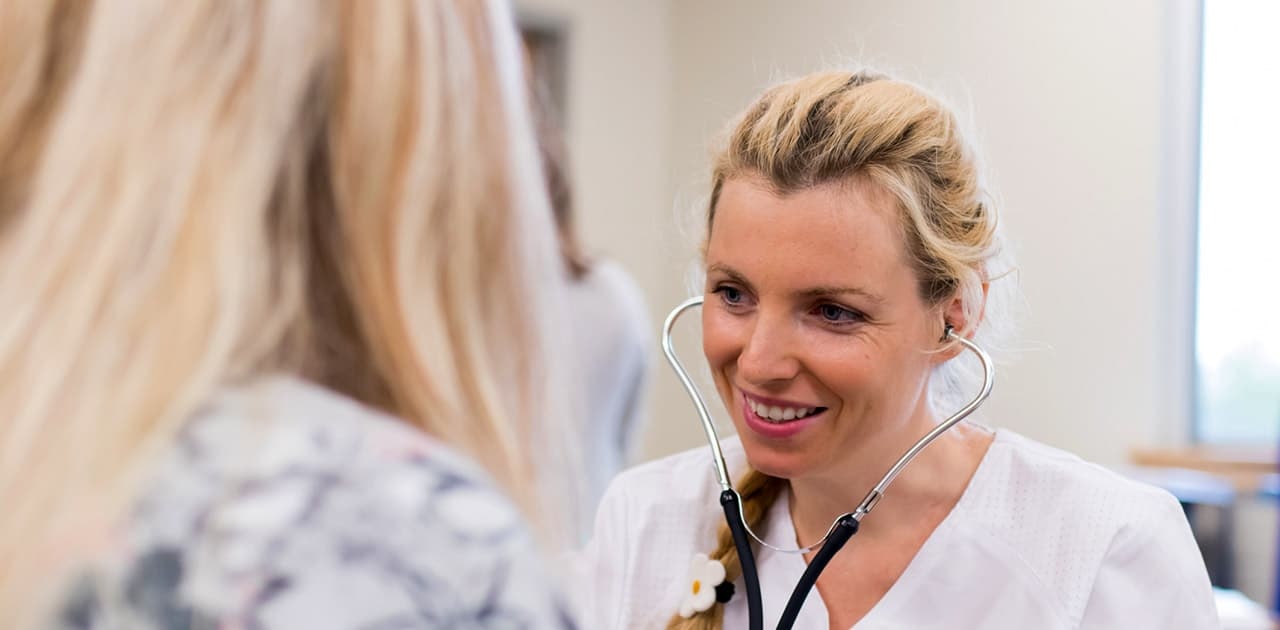 a nursing student listens to another student's heartbeat using a stethoscope