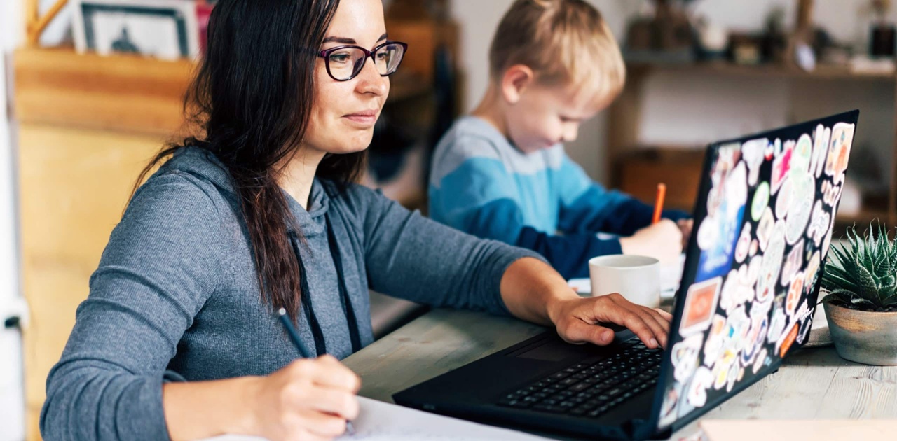 mom wearing glasses works on a course online as her son plays in the background