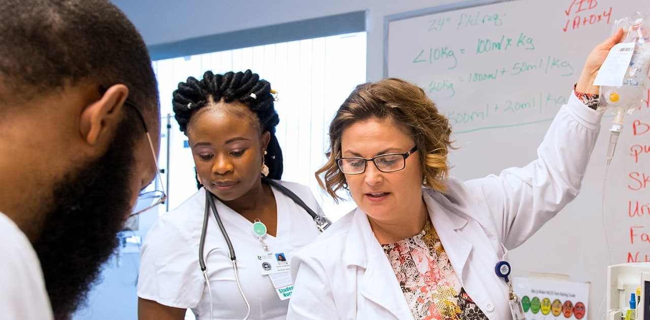 a nursing professor demonstrates to students how to administer an IV