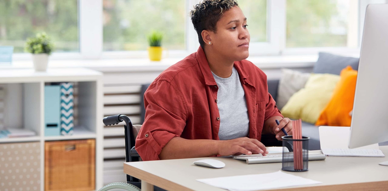 female student of color using a wheelchair works on her iMac at her desk