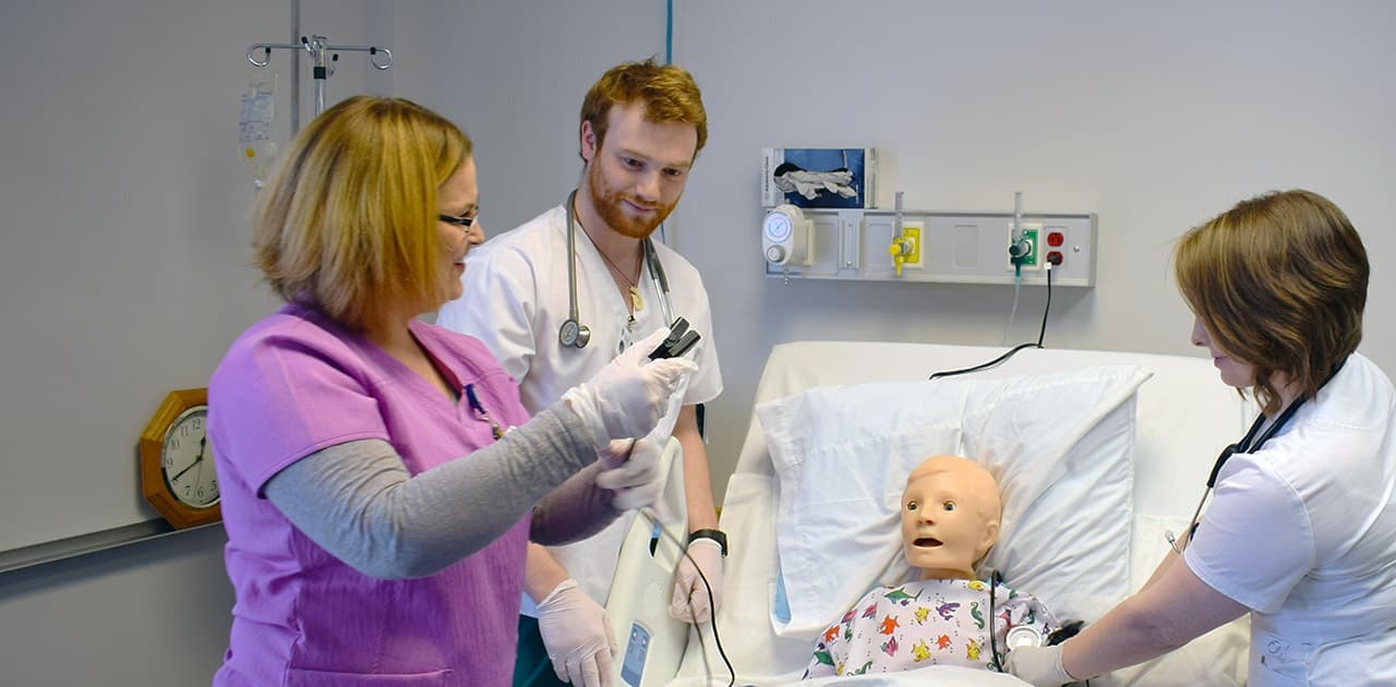 a nursing professor demonstrates to nursing students using a practice mannequin